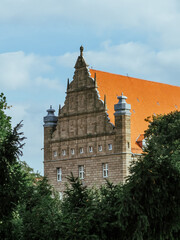 Zabytkowy ozdobny szczyt kamienicy z jasnego kamienia z jasnopomarańczowym dachem © Szymon
