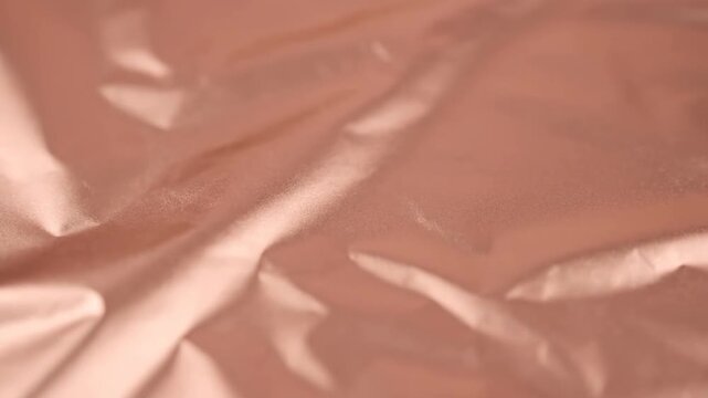 Abstract blurred background of crumpled metallic rose gold foil texture. Macro shot showing smooth wrinkles and reflective shiny material surface for modern graphic design.