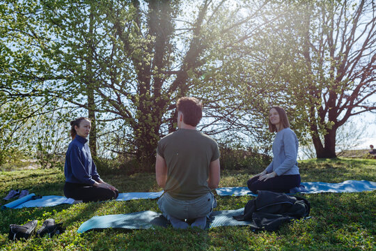 Three Friends Sitting on Yoga Mats Talking Before Outdoor Meditation Session