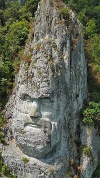 Aerial around view of stone carved statue portrait of ancient dacian king Decebal. Sculpture near Danube River, Romania. Vertical video 4k