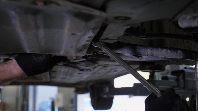 An auto mechanic is working on a car under the car lift in the garage. The auto repair shop is repairing the bottom of the car with modern auto repairs.