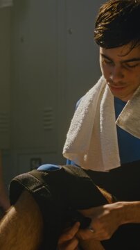 Athlete Focused on Adjusting Protective Knee Sleeve, Preparing For Football Practice in Locker Room. Self Care Routine of Student Athletes Managing Joint Protection, Physical Readiness. Vertical Shot.
