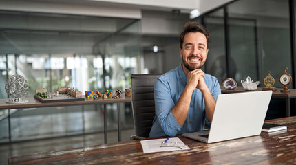 Fototapeta premium Successful Man Working at Laptop in Modern Office with Creative Decorations and Glass Walls