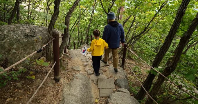 Father and son holding hands, climbing down rough stone stairs through mountain forest, returning from Ulsanbawi Rocks in Seoraksan National Park. Follow shot captures quiet bonding during trip