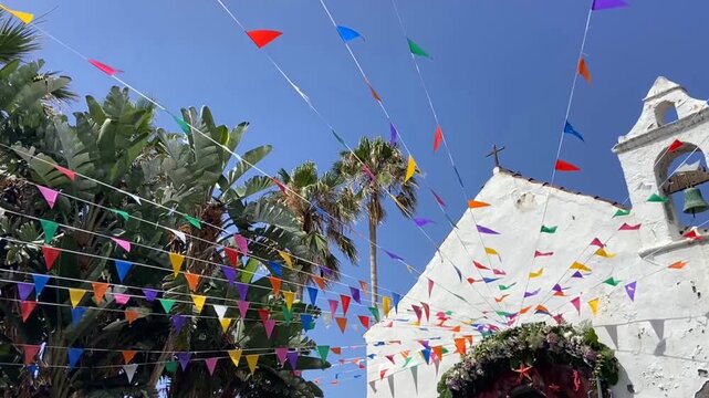 Ermita de San Telmo church with multicolored triangular small flags to holiday celebration and palm trees against blue sky in in Puerto de la Cruz, Tenerife, Canary islands, Spain,4K.