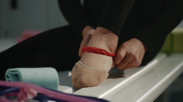 Close Up of Rhythmic Gymnast Foot in Specialized Half Socks Inside Changing Room. Athlete Meticulously Ties Red Elastic Resistance Band Around Arch and Ankle, Likely For Injury Prevention, Support.