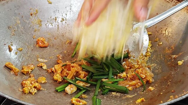 Adding fresh bean sprouts and Chinese chives to Pad Thai noodles in a wok.