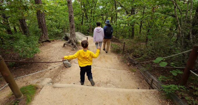 Boy follows behind while mother and father walk ahead holding hands. Tourist family navigates pathway through green autumn forest, enjoying scenic hiking experience in Seoraksan National Park.