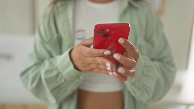Woman holding a red smartphone and showing fingernails while texting inside building near vote sign; civic pride.