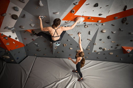 Two female climbers work on route in indoor bouldering hall. Image for partnership, technique, confidence, challenge, fitness branding, recreation promotion
