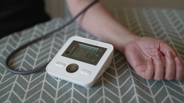Woman measuring blood pressure with digital monitor at home.