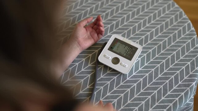 Woman measuring blood pressure with digital monitor at home.