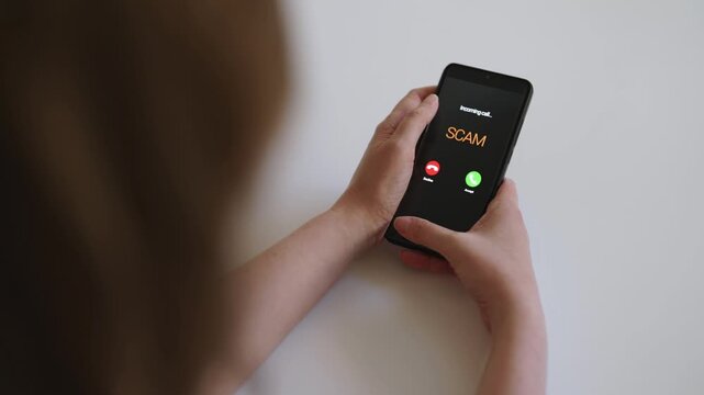 Woman holding smartphone with incoming scam call on screen.