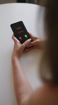 Woman holding smartphone with incoming scam call on screen.