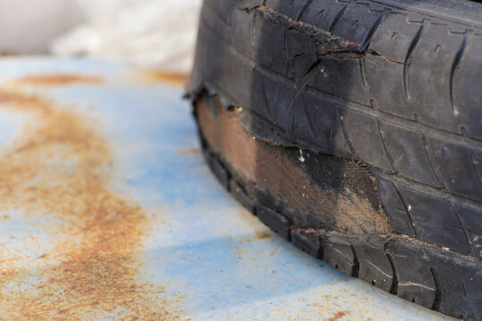 Severely Damaged Old Car Tire with Exposed Cords Resting on Rusty Surface