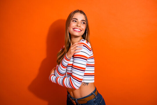 Young stylish woman smiles wearing striped top posing against vibrant orange background for lifestyle fashion shoot
