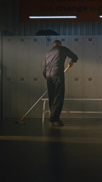Male Cleaner in Black Overalls is Methodically Mopping Floor of Empty Locker Room. Man Stops Working, Picks Up Left Behind Soccer Ball, Starts Skillfully Juggling it With Feet and Knees. Vertical Shot