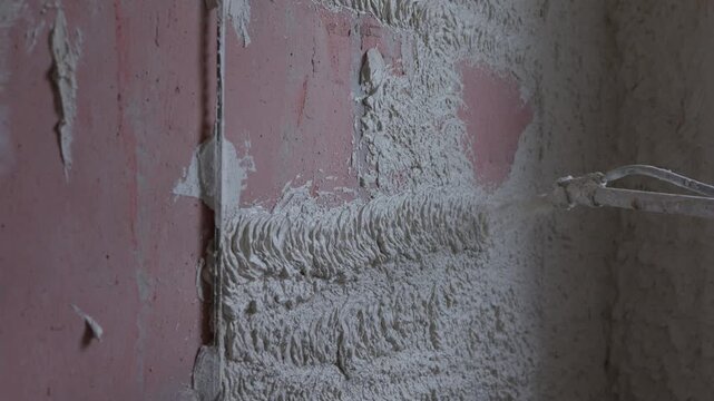 Machine applying cement plaster to interior wall during construction