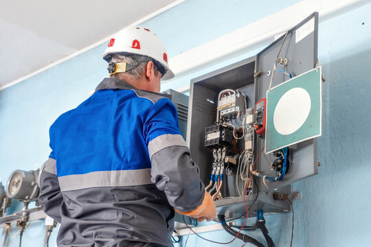 Electrician in a safety helmet working on a control panel with various electrical components. Electrical maintenance and repair service.