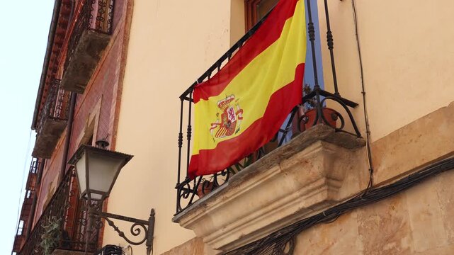 Spanish national flag with coat of arms waving on a balcony supporting the football team on a historic building in Spain