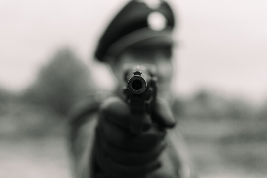 Black and white retro shot of a pistol aiming forward with a blurred soldier in the background.