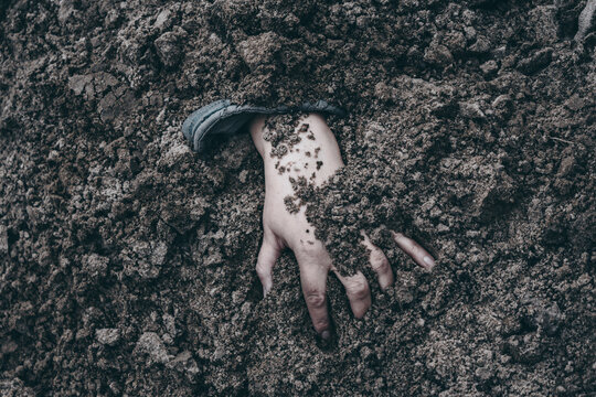 The concept of investigating war crimes. Buried human hand reaching out from dark clumpy soil. Symbol of mass grave, genocide, war crimes, and tragic historical memory.