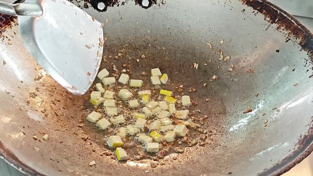 Stir frying diced yellow tofu with garlic and shallots in a wok.