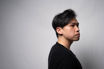 Profile portrait of a thoughtful young Asian man in a black shirt looking away against a light grey background with copy space © Freddy Chandra