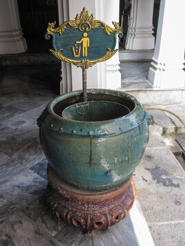 Bangkok, Thailand. December 14, 2013, Green ceramic waste bin with a vintage gold and green sign for discarding trash, standing on an antique base near temple architecture