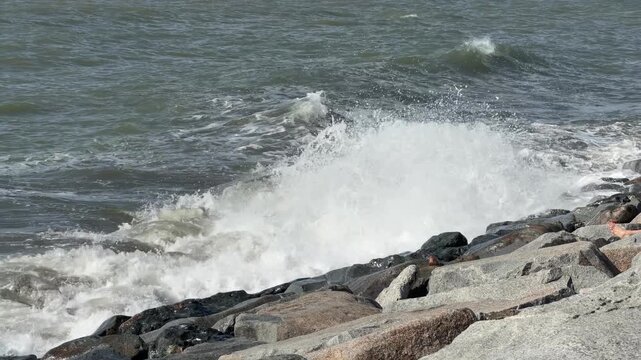 Powerful ocean waves crash against a rocky shoreline with white foam and spray.Dynamic sea waves surge and break against a rugged coastal barrier, creating a dramatic natural display of water and ston