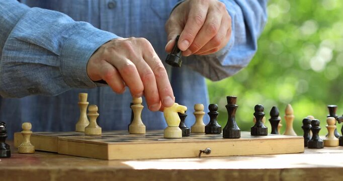 Male playing chess game on wooden vintage chess board on nature outdoor, strategy and logic leisure activity or intellectual hobby.