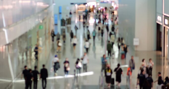 Real-time elevated view of moderately busy airport terminal corridor with intentionally defocused passengers walking past duty-free stores, anonymized motion captures essence of modern travel