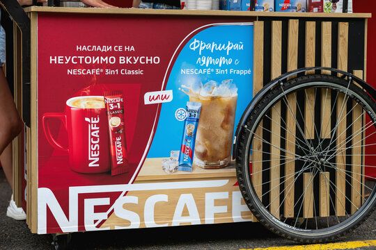 Nescafe coffee kiosk displays hot and iced drink advertising at sport event. Coffee promotion uses branded counter beside bicycle wheel and service area