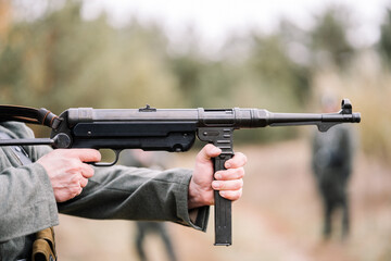 Obraz premium Close-up of hands firing an MP-40 submachine gun during a historical reenactment. 