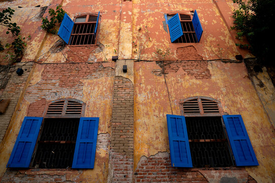 Old Heritage Building Facade with Peeling Orange Plaster and Vibrant Blue Wooden Shutters