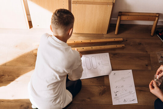 Close-up of kid's assembling flat pack furniture at home. DIY lifestyle scene showing home improvement, manual work, and furniture installation in natural light