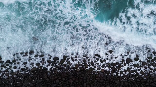 Top down drone view of waves washing over stone pebble beach. Water texture and foam details background footage