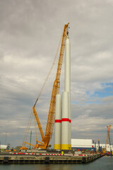 Fototapeta premium Giant Crawler Crane Assembling Wind Turbine Tower Sections at Port Harbor, Sustainable Offshore Renewable Energy Construction and Logistics