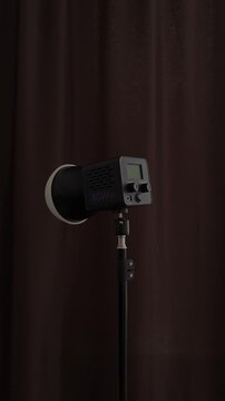 Turning off 40W LED video light on stand - studio lighting demonstration. Vertical footage of hand turning off a 40W LED video light on a stand. Unit powers down against brown curtain, ideal for studi