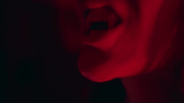 Close Up View of Young Woman Pressing Artificial Vampire Fang Into Place During Halloween Costume Preparation Under Red Light, Horror Style, Festive Celebration