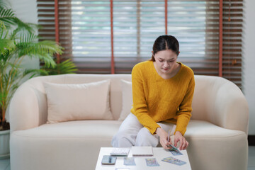 Asian woman managing personal finances at home, counting cash money and calculating expenses on a...
