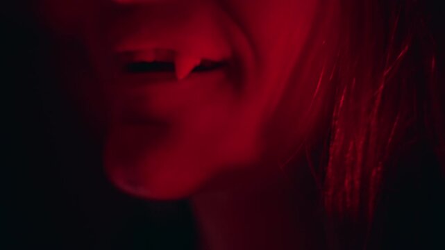 Close Up View of Young Woman Showing Tongue With Artificial Vampire Fangs Under Red Light, Halloween Costume Preparation, Horror Theme, Playful Expression