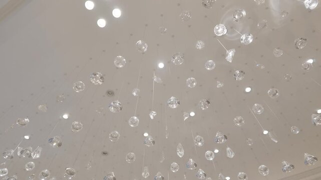Low angle abstract shot with a slow camera pan right showing a luxurious modern light installation with hanging glass crystal balls on an elegant warm-toned ceiling.
