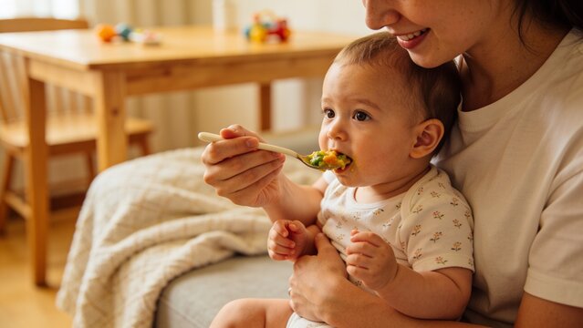 Baby eating healthy meal from mother&rsquo;s spoon during a peaceful family feeding time.