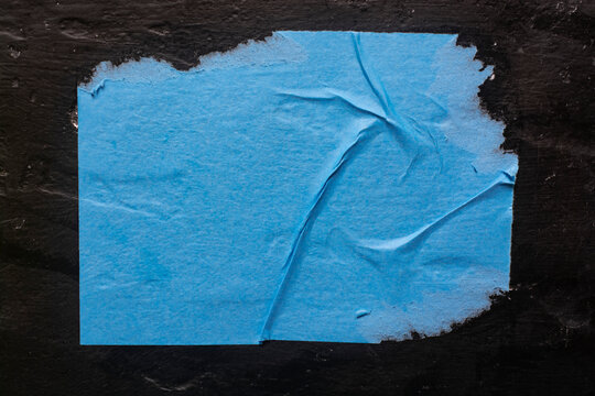 Old torn blue poster with folds on black background