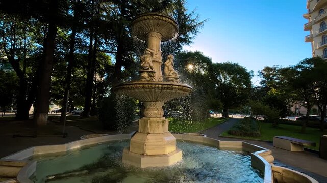 View of city street of Batumi with old angel fountain with cupid statues at sunrise - early morning, clear blue sky and sun lens flares