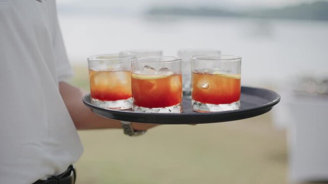 A server carrying a tray of refreshing iced cocktails, featuring vibrant orange layers and citrus garnishes, perfect for summer parties, hospitality, and celebration concepts at a luxury resort.