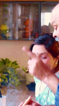 Active Indian Asian senior couple sharing a joyful moment in the kitchen, with the husband explaining a recipe while the wife admires his culinary skills and the aroma of hot food