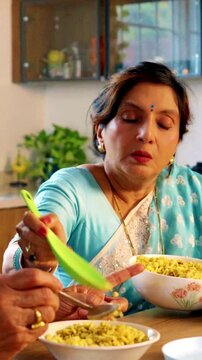 Joyful Indian Asian senior couple enjoying their evening snacks together at the dining table in their modern kitchen engaged in lively discussions and cheerful chatting