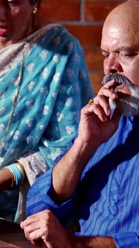 Asian Indian elderly couple with sad, disappointed expressions reviewing a drop in retirement investment returns at night in their home